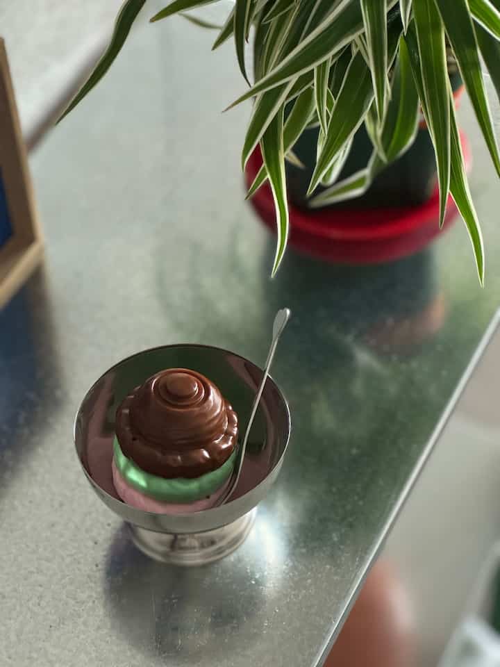 A silver-tone stainless steel ice cream bowl with a heart-shaped fork on a kitchen table featuring a cute ice cream model