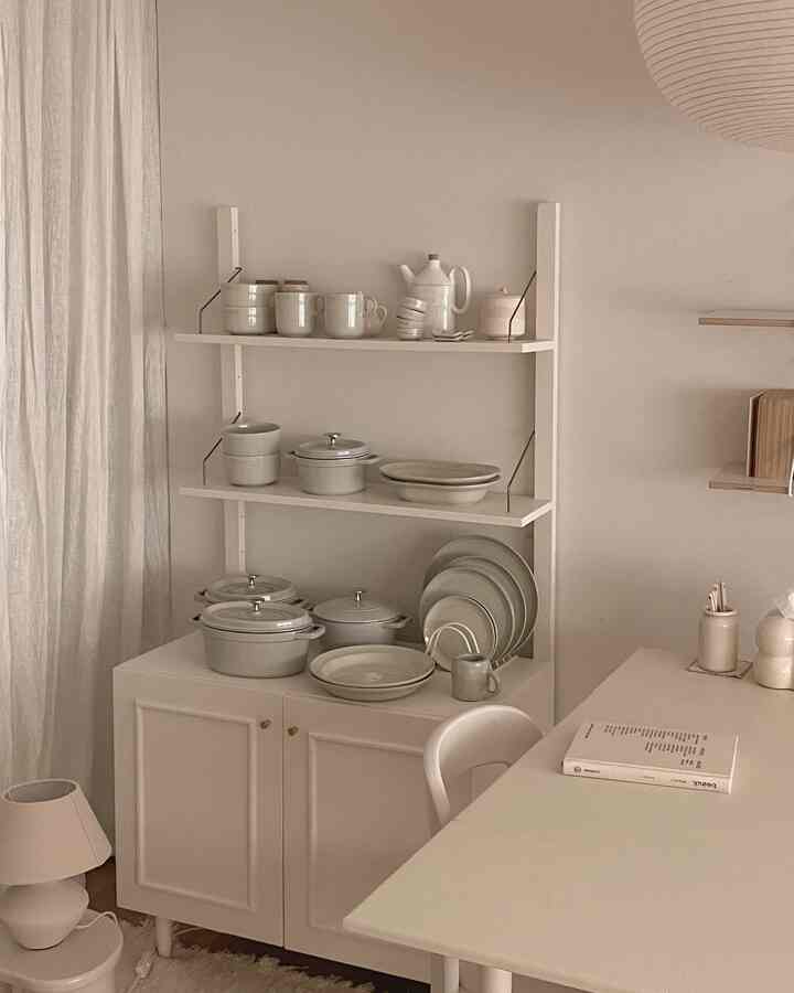 ホワイトとベージュの色調のキッチンスペース、棚とキャビネットに整然と並べられたキッチン用鍋と皿があるシンプルなインテリア