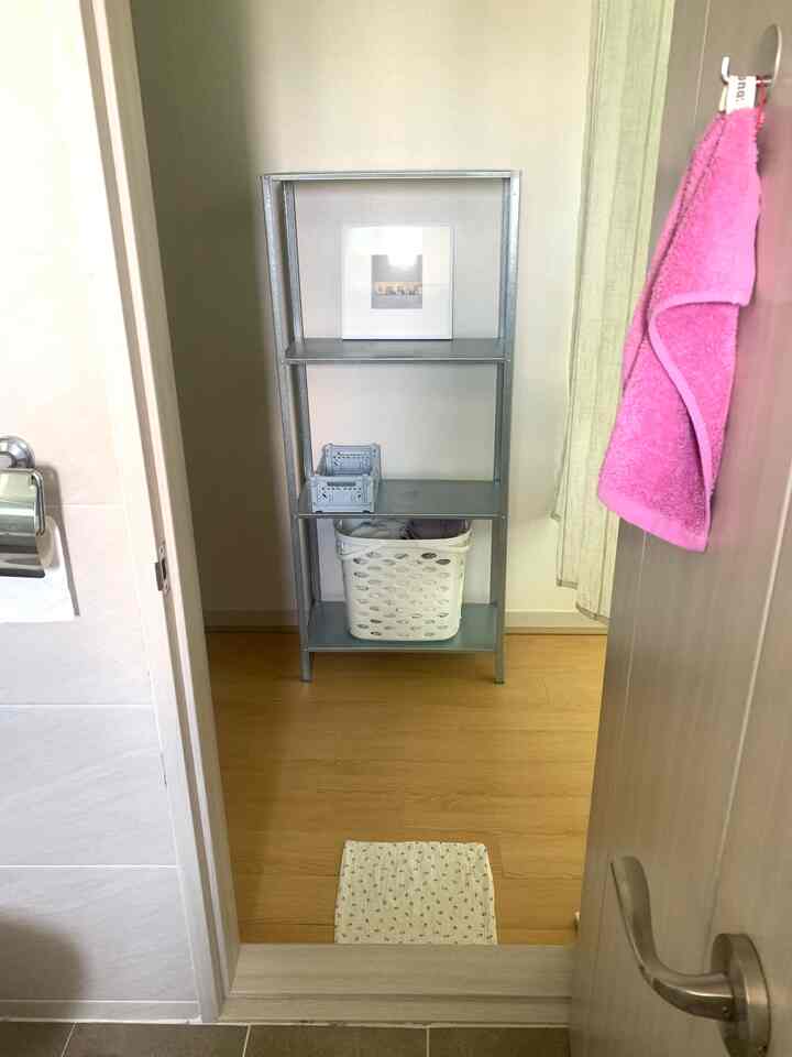 白を基調としたバスルーム入り口前にイケアの鉄製棚とピンクのタオルがある実用的なワンルームの収納スペース