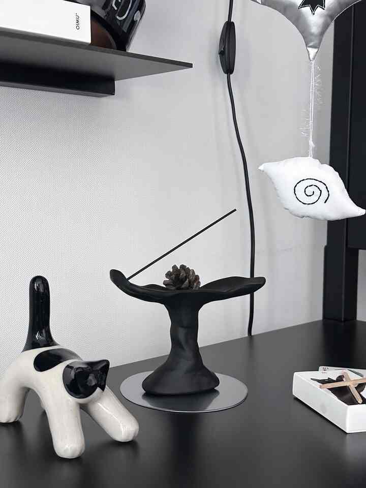 ブラックとホワイトのモノトーン空間に、ミニマルなデザインのマットブラックのインセンスホルダーと猫のオブジェが配置された洗練されたインテリア小物