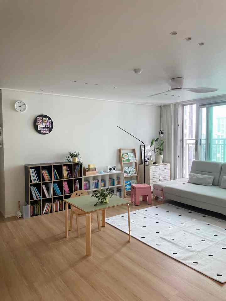 Living room with white walls and wood-tone floors featuring a 4-person sofa, kids' desk, and multi-tier bookshelves in a cozy atmosphere