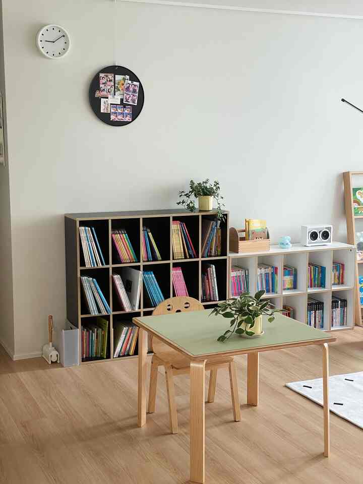 Natural tone kids' room with white walls and wood-tone flooring, featuring wooden table and children's bookshelves arranged neatly