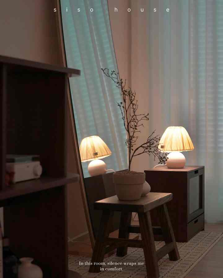 Cozy bedroom corner with natural wood tones featuring a small stool with plant and warm lamp lighting