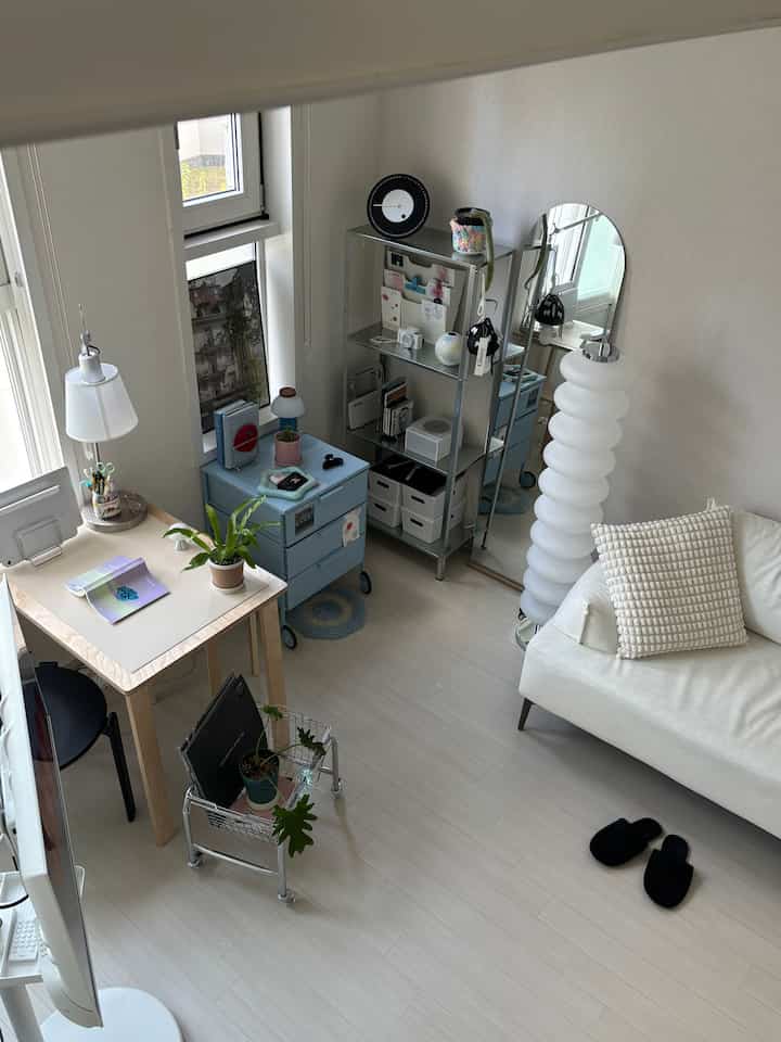 明るいホワイトとウッドトーンのワンルーム、机とソファ、棚、フロアランプが配置された落ち着いた印象的な空間