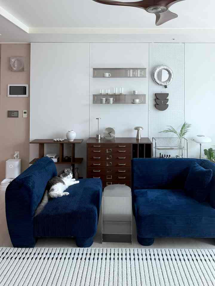 ネイビー色のモジュールソファが際立つリビング、木製家具や棚、壁時計、ラグが配置された雰囲気のあるインテリア