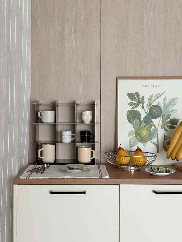 Natural wood-tone wall and white kitchen cabinets with cups and a fruit basket create a cozy kitchen space