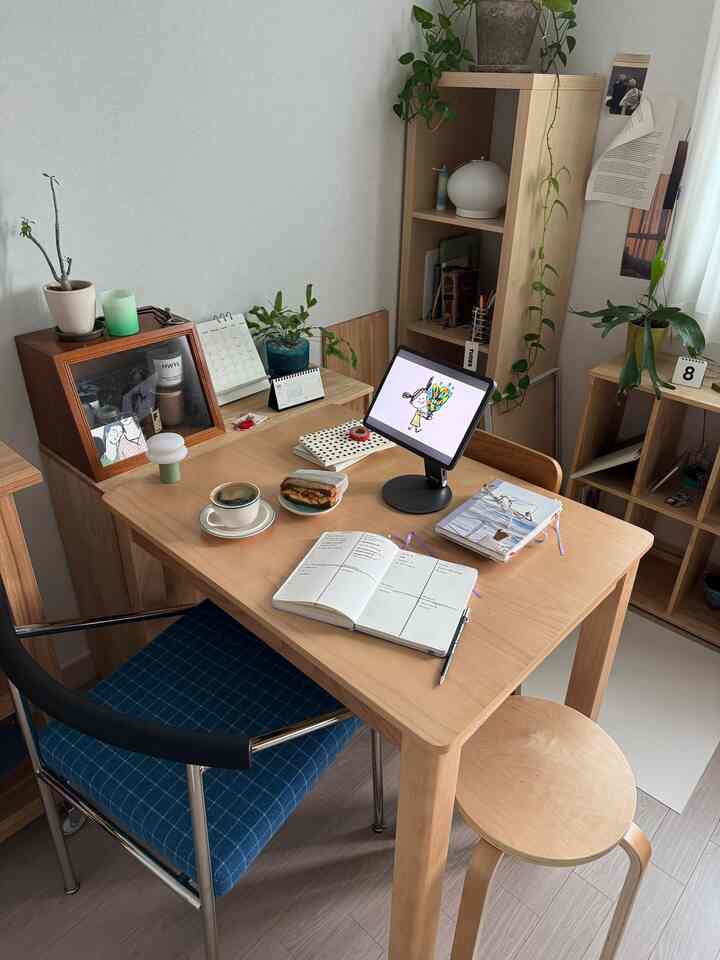 ナチュラルな色調のダイニングルーム、デスクとスツール、本棚が配置された落ち着いた印象的な空間