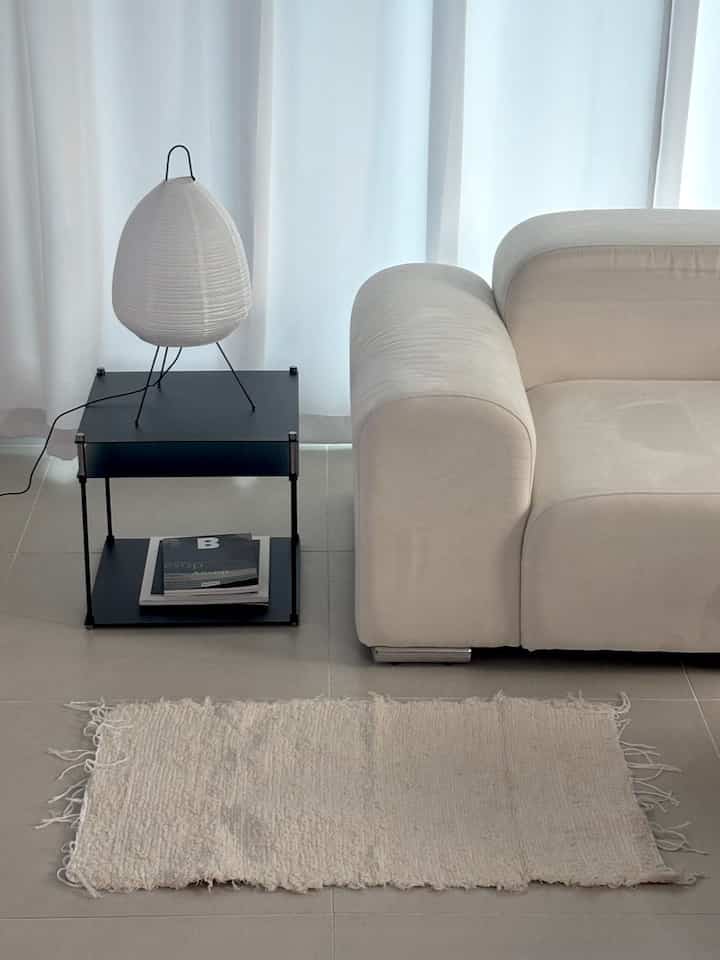 A simple living room in white and black tones featuring a sofa, black side table, and a cozy white rug creating a clean interior.
