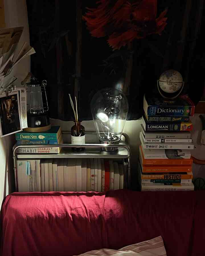 暗いトーンのレトロスタイルの寝室の一角、中央にワイヤレスムード照明と本棚、赤いベッドカバーが配置された落ち着いた空間