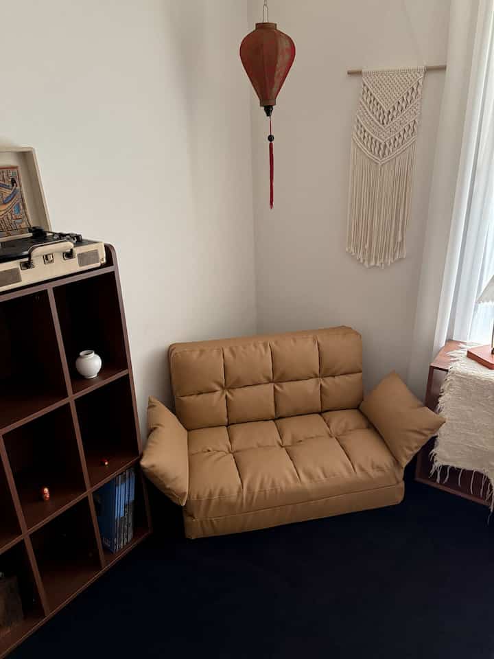 暖かみのあるブラウンのソファベッドと黒いラグ、ナチュラルなウォールデコが配置された居心地の良いリビングスペース