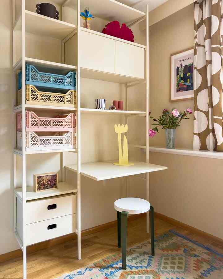 Cozy natural-toned small room corner featuring a foldable white desk and stool with patterned curtains