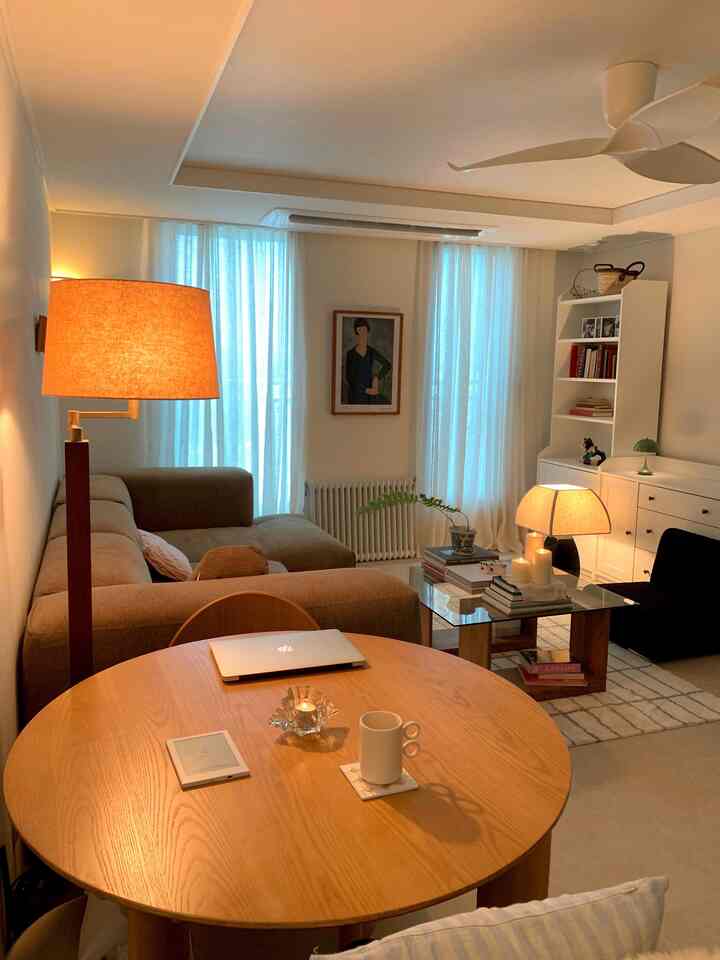 温かみのあるナチュラルカラーのリビング、ソファと丸い木製テーブル、照明で雰囲気のあるインテリア