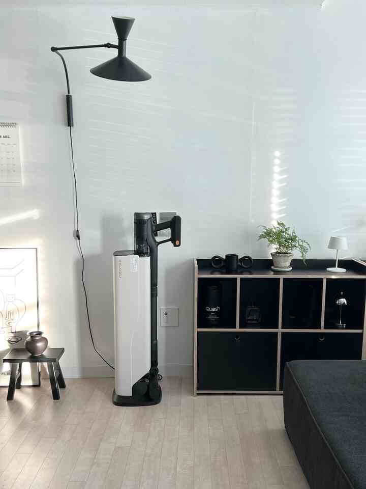 白い壁とモノトーンの家具が配置されたリビング、コードレス掃除機とドッキングステーションが中心にあり、清潔感のある雰囲気のインテリア