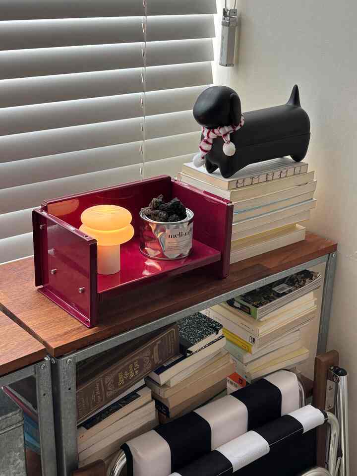 白いブラインドを背景に、ナチュラルカラーの棚と赤い小物が調和した読書スペース