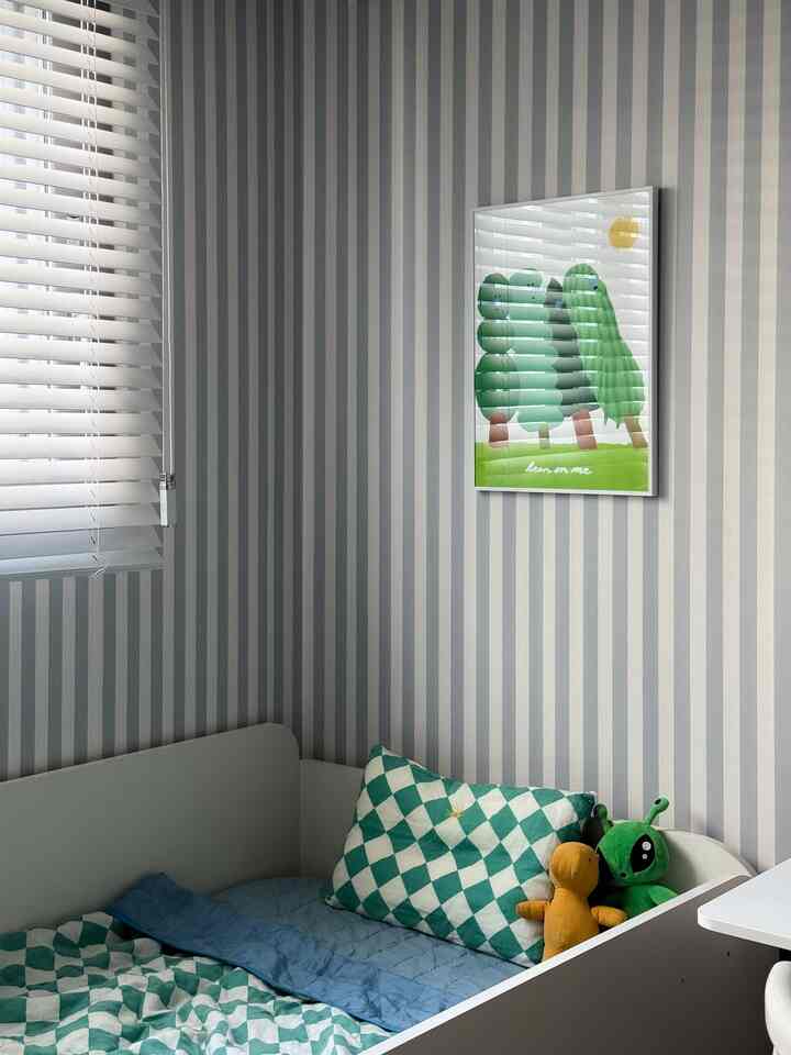 グレーと白のストライプ壁紙の小さな寝室、白いウッドブラインドと子供用ベッド、おもちゃが配置された落ち着いた雰囲気のインテリア