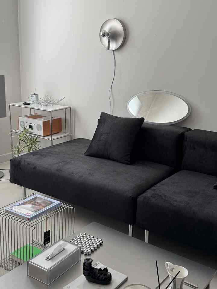 モダンな黒のソファとシルバーの壁照明が配置された、すっきりとしたリビングルームのインテリア