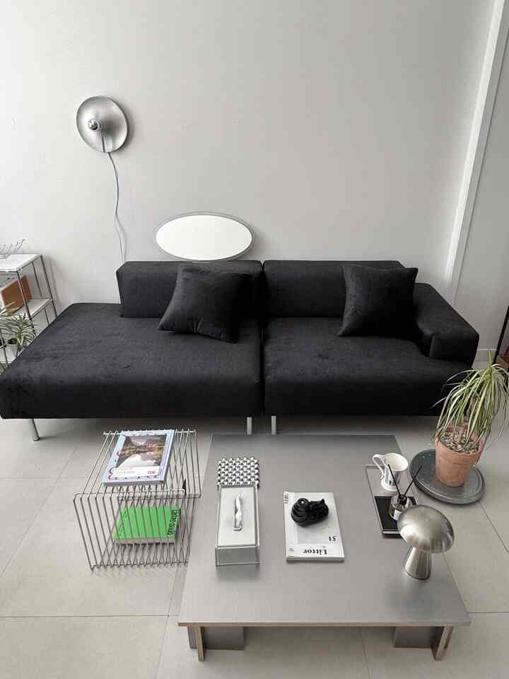 黒いファブリックソファとシルバーのコーヒーテーブル、壁掛け照明が配置されたミニマルなリビングスペース