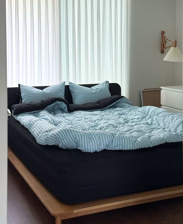 Natural modern bedroom in white and black tones featuring blue striped bedding and wooden bed frame, creating a cozy atmosphere