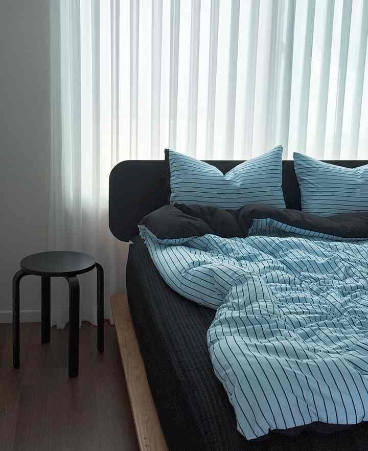 Modern and clean bedroom with black and white harmony featuring blue striped bedding and a black stool