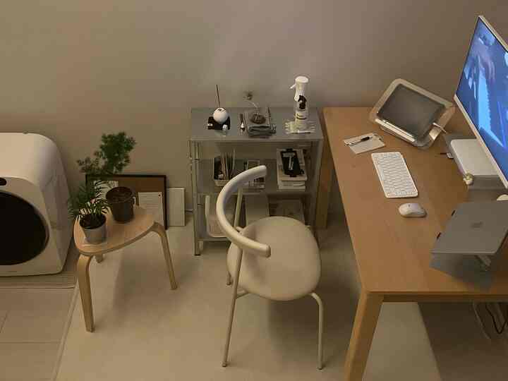 A clean home office with natural wood tones and white colors, featuring a desk, chair, shelf with small plants in a neat layout