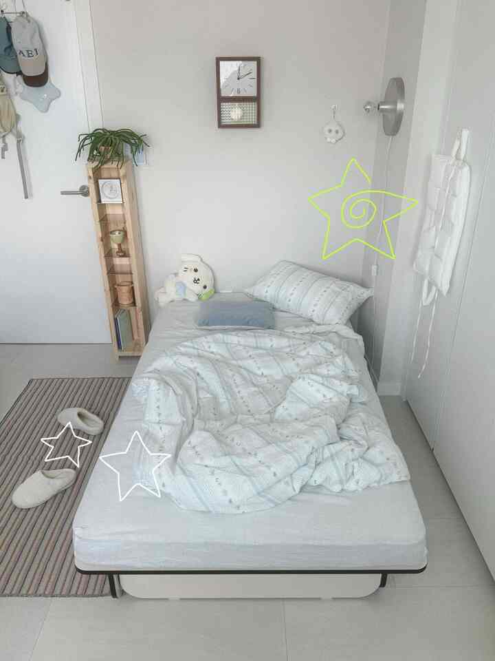 ホワイトとベージュのトーンが調和したワンルーム寝室、シンプルなベッドと壁照明が配された印象的な空間