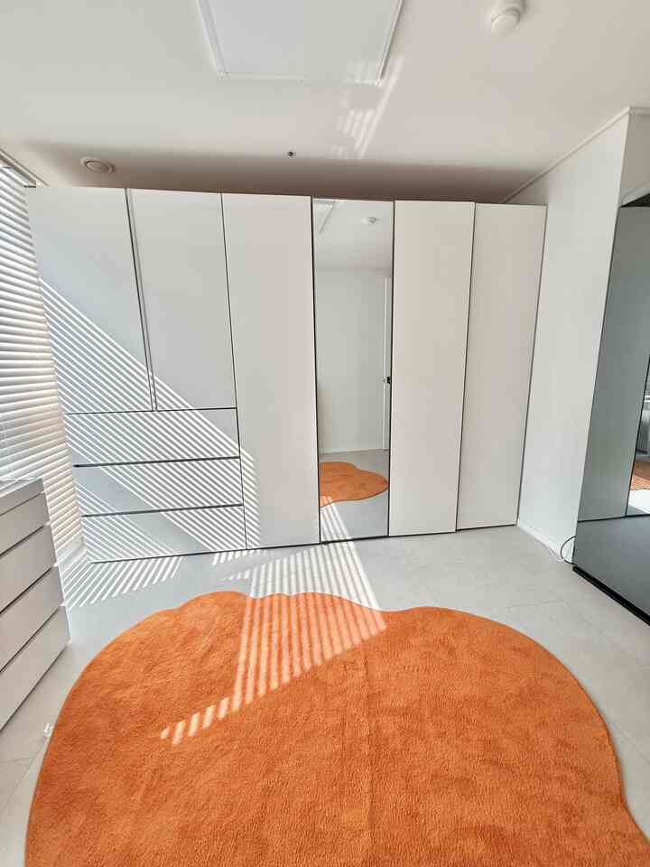 明るいウッドトーンとホワイトのクローゼットがある部屋、不規則な形のオレンジラグが配置された清潔感のある空間