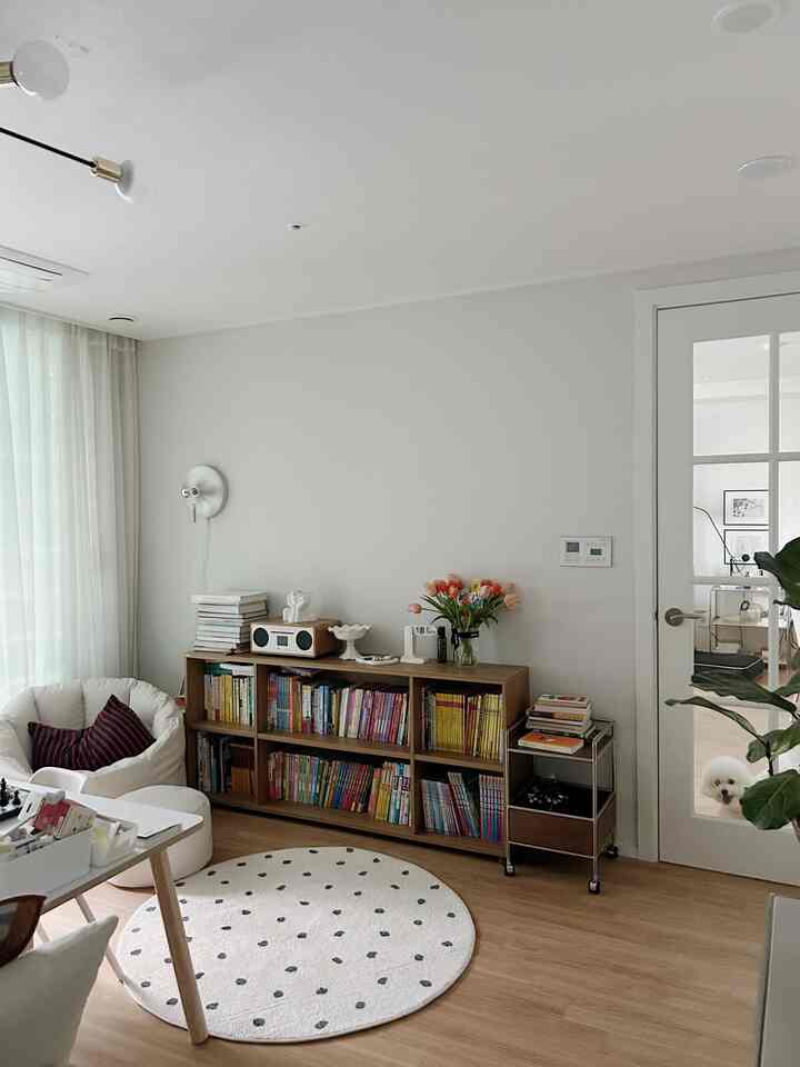 ナチュラルモダンで北欧風のリビングルーム、本棚やビーンバッグ、ラグが配置され、ガラス扉越しにホームオフィスが見える雰囲気のあるインテリア