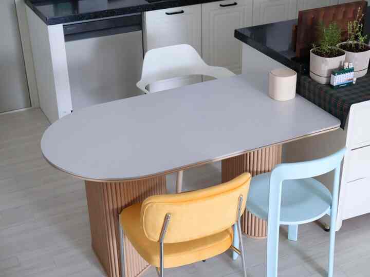 ライトグレーの天板と木目調の脚があるキッチンダイニング、三色の椅子が配置された清潔感のあるコンパクトな家のインテリア