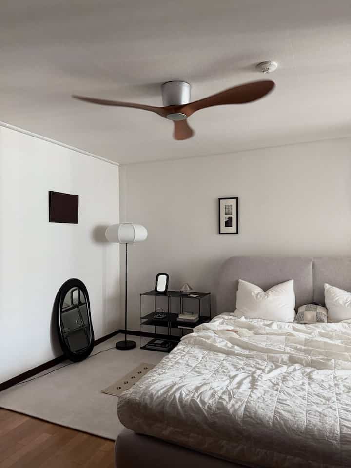 A modern bedroom in white and black tones featuring a bed, floor lamp, mirror, and minimal decor