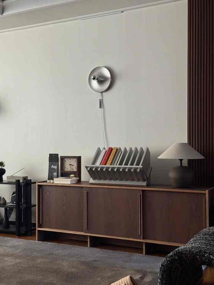 チャコールカラ―のラグと濃いブラウンのリビングキャビネット、シルバーのUFO壁灯が配置されたモダンなリビングルーム