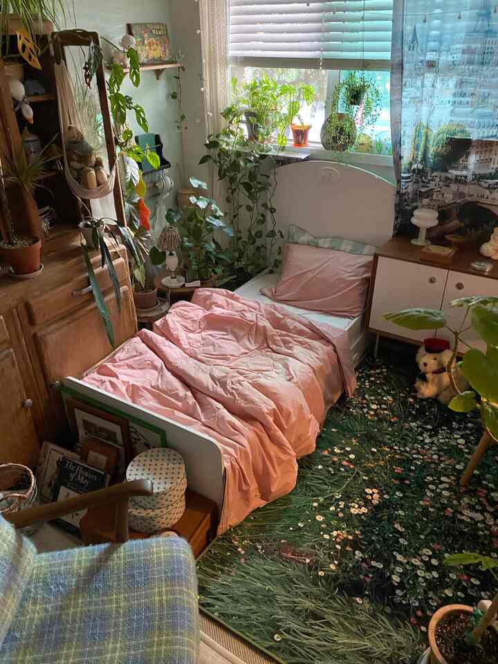 ピンクの寝具と緑の植物が調和した居心地の良い寝室、木目調の家具と花柄のラグが配置された自然な雰囲気のインテリア
