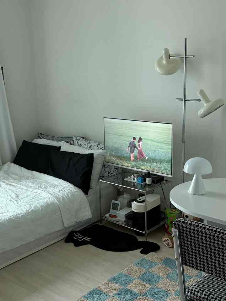Studio apartment bedroom in white and black tones, featuring a bed, TV, and dining table arranged in a compact home cafe style interior
