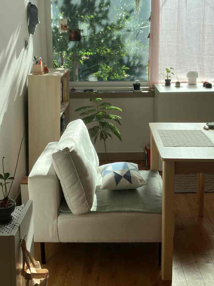 自然光があふれるコンパクトなリビングルーム、木製ダイニングテーブルと植物、白いソファが配置されたナチュラルでミニマルな空間