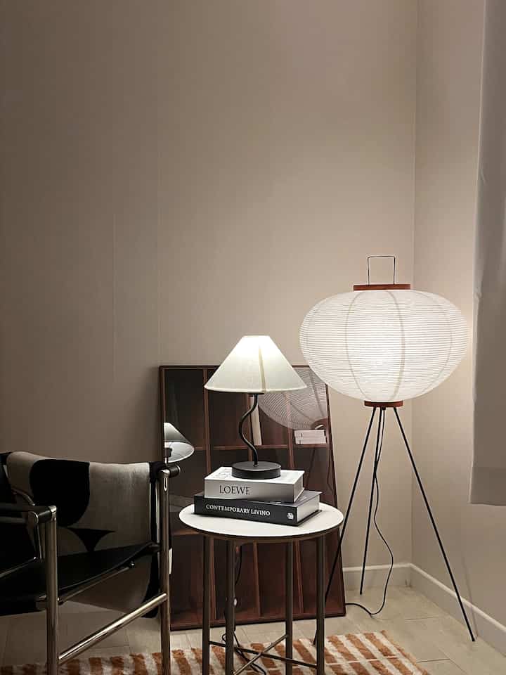 ベージュ色の壁とナチュラルカラーの寝室コーナー、サイドテーブルとさまざまな照明が配された雰囲気のあるインテリア