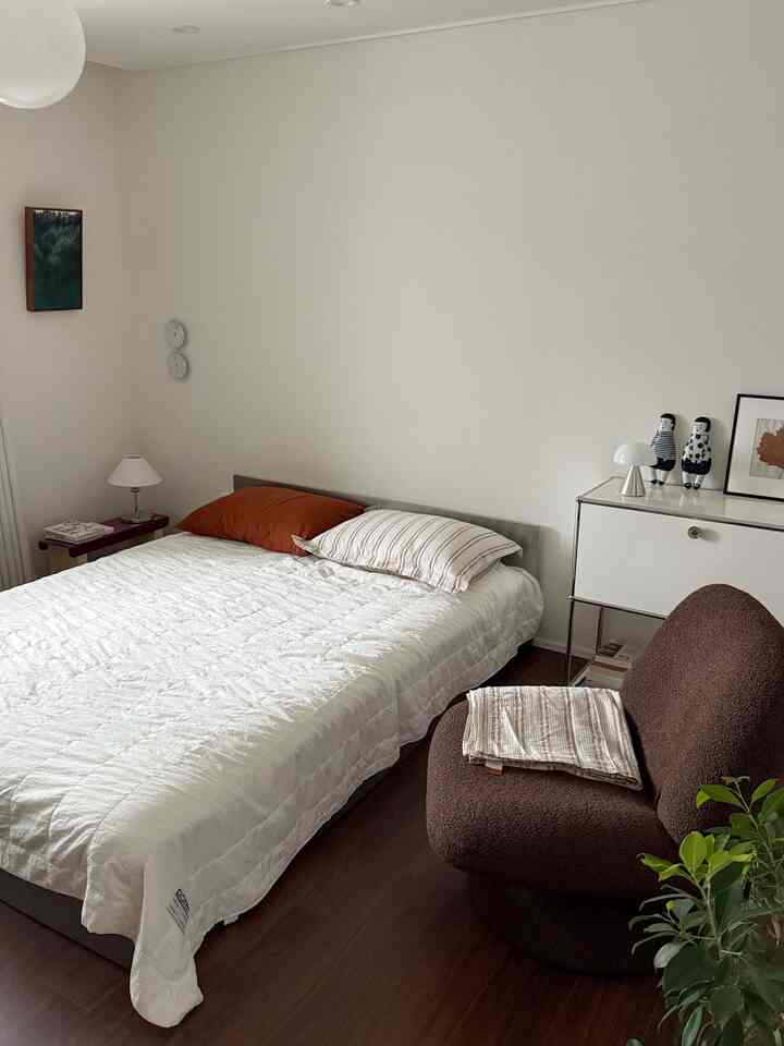 Natural modern bedroom with white and brown tones, featuring a simple bed and cozy armchair for a calming atmosphere