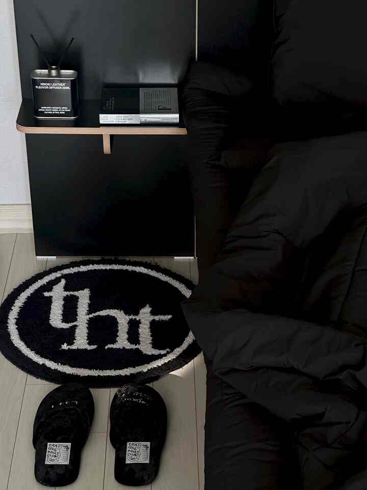 無彩色の寝室、黒い寝具とスリッパ、円形のラグが配置されたシンプルなインテリア