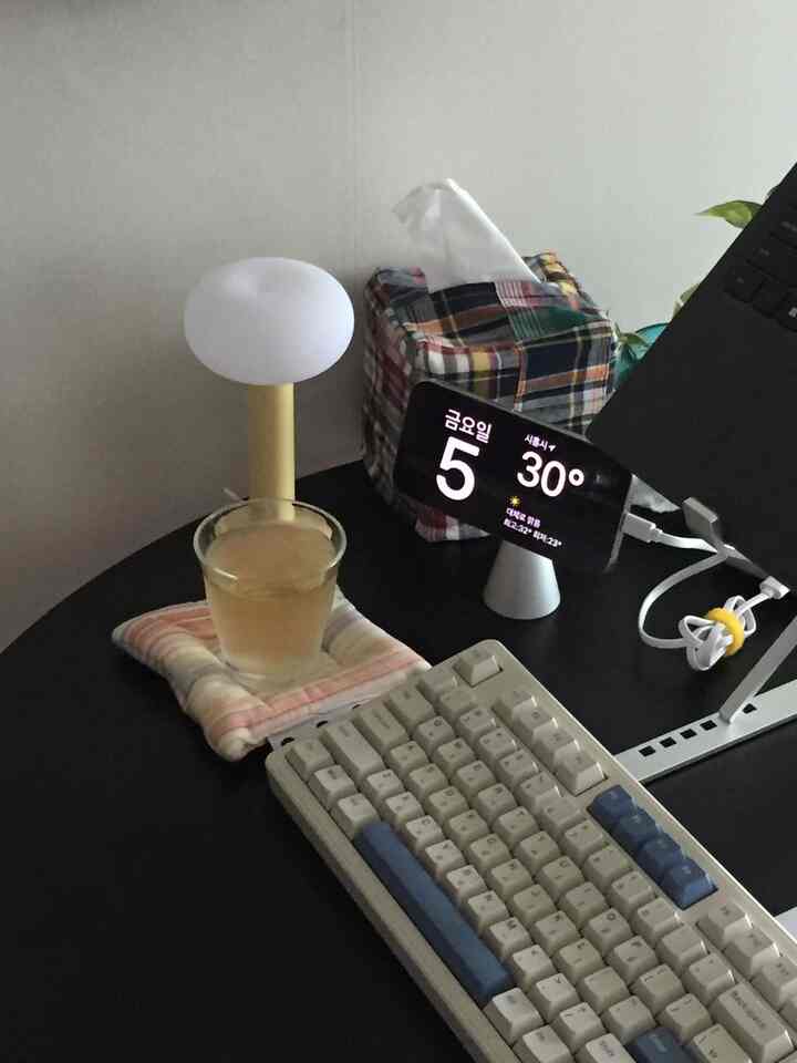 ブラックトーンのホームオフィス空間、丸いデスクにキーボード、テーブルランプ、スマホスタンドが配置された整った作業環境