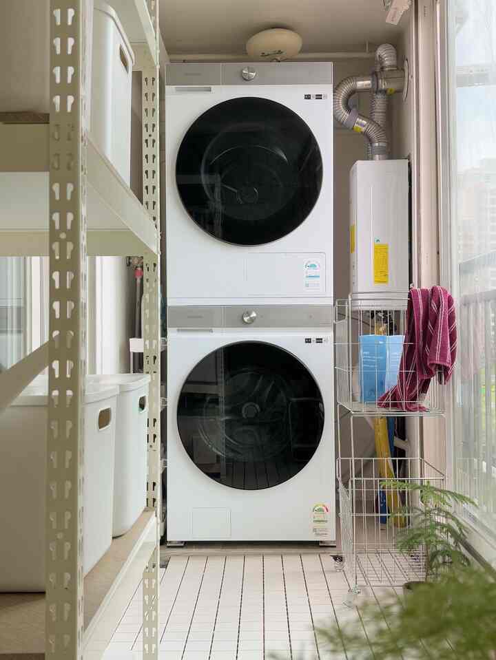 ホワイトトーンの狭いランドリースペース、積み重ねられた洗濯機と多機能収納棚が配置された清潔な実用的空間