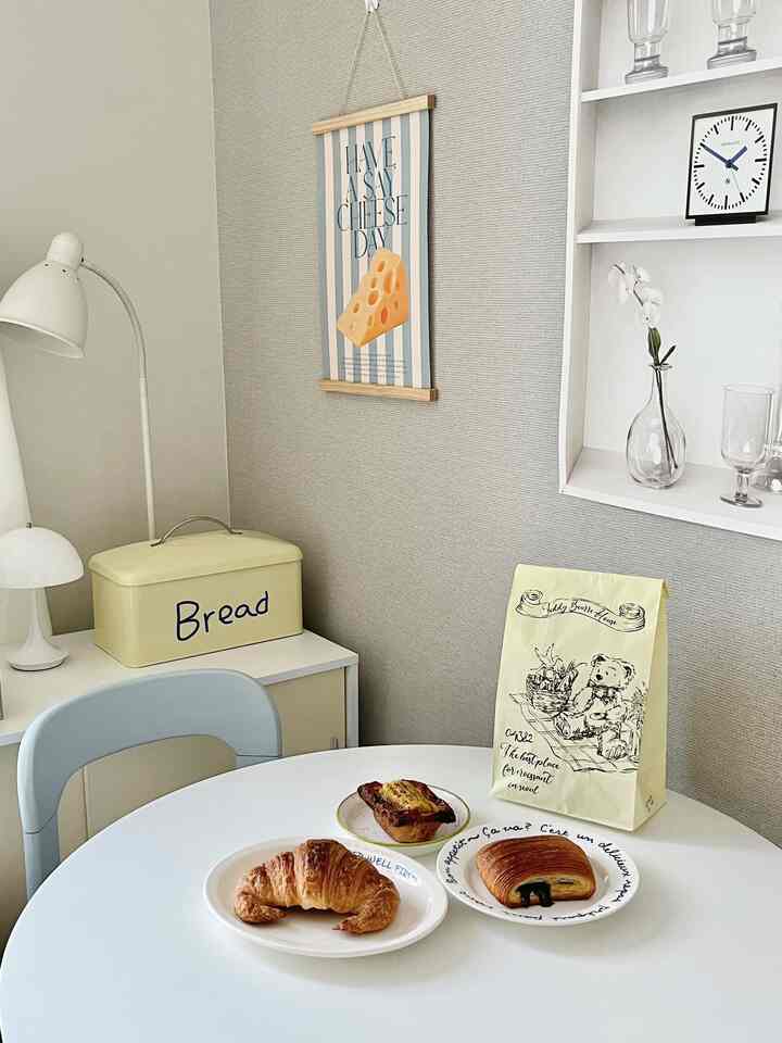 白とナチュラルカラーの小さなダイニングルーム、丸テーブルにパンやポスターが置かれた雰囲気のあるカフェ風の空間