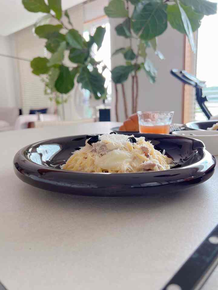 ホワイトトーンのダイニング、食卓には料理とグラスが配置され、背景には大きな植物があるシンプルな空間