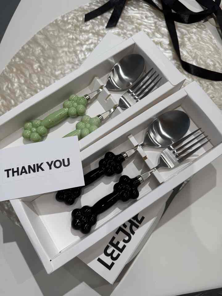 グリーンと黒の持ち手が特徴的なカトラリーが、白いテーブルマットの上に箱に整理されたキッチン用品の画像