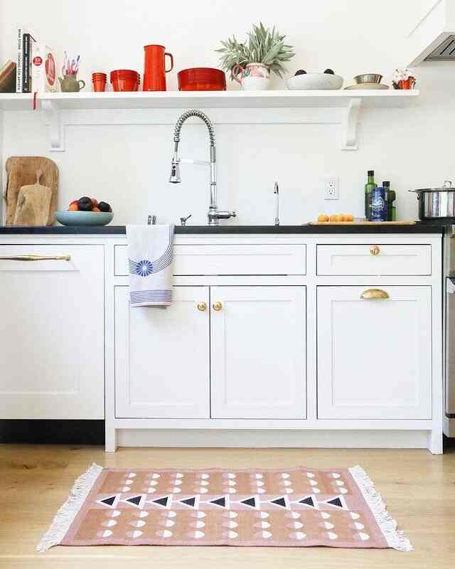 White and natural toned kitchen with black countertop and gold handles, featuring a clean and fresh aesthetic