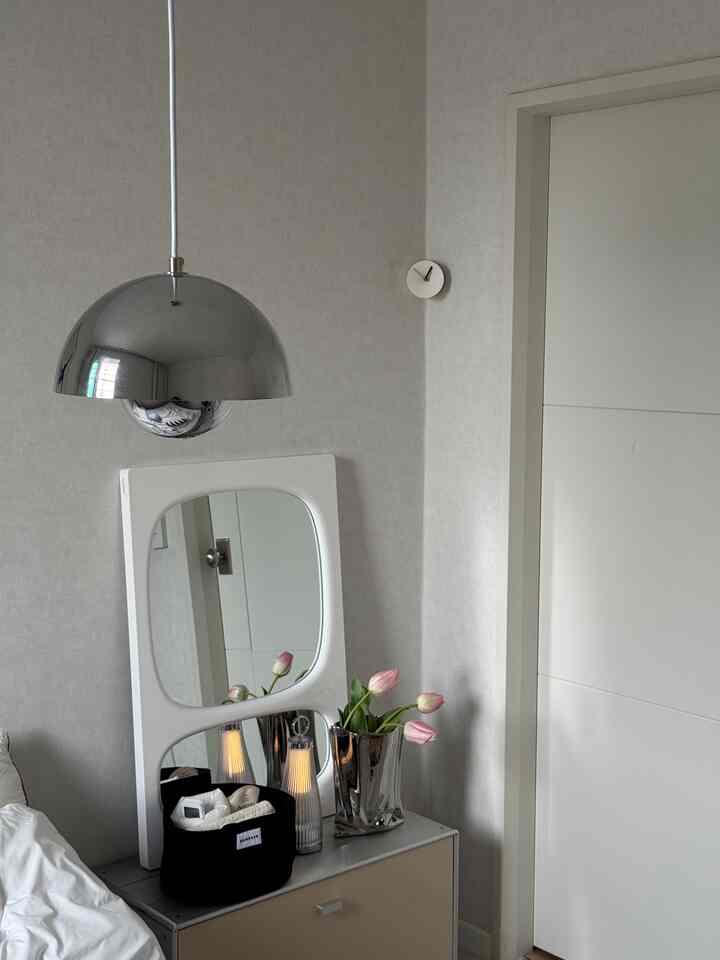 白とシルバーのトーンの寝室、中央にペンダントライトと鏡、花瓶が配置された洗練された印象的な空間