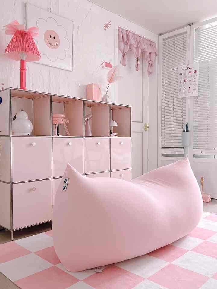 ピンクと白のトーンのリビングルーム、中央にピンクのビーンバッグと収納が配置された居心地よくシンプルな空間
