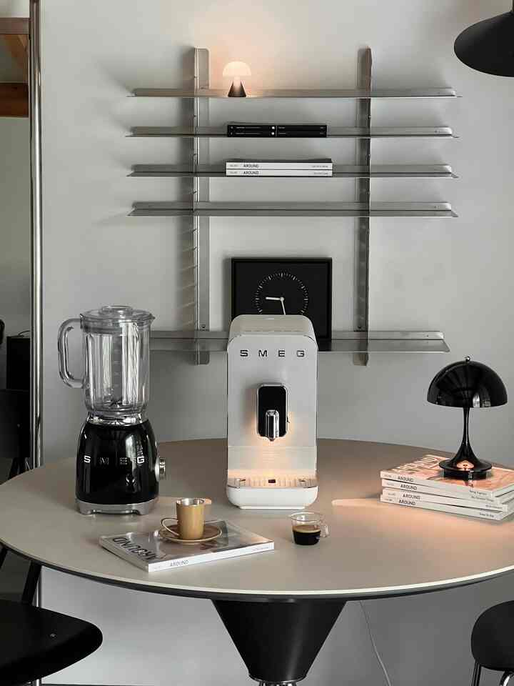 白と黒のトーンでまとめられたミッドセンチュリーモダンのワンルーム、ダイニングテーブルにコーヒーマシンとブレンダーが配置されたシンプルモダンな空間