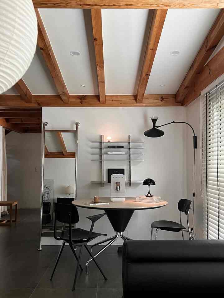 ウッド調の梁が印象的なモダンなブラックインテリアのホームカフェ空間、ラウンドテーブル中央にスメグ全自動コーヒーマシン配置