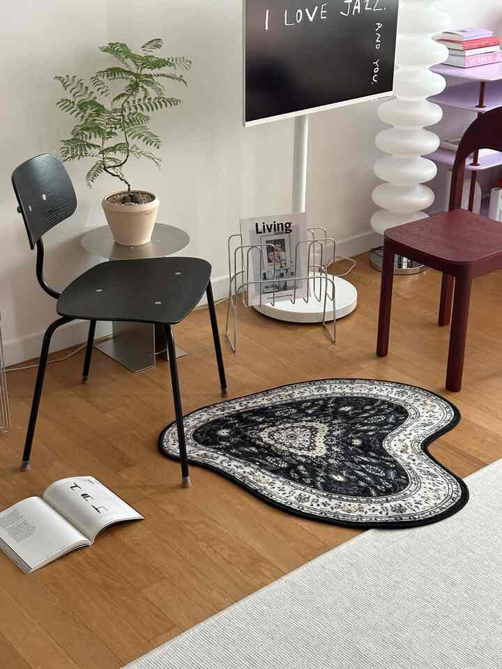 ライトブラウンの木製床、黒い椅子、ハート型の黒いラグが配置されたモダンなリビングルーム