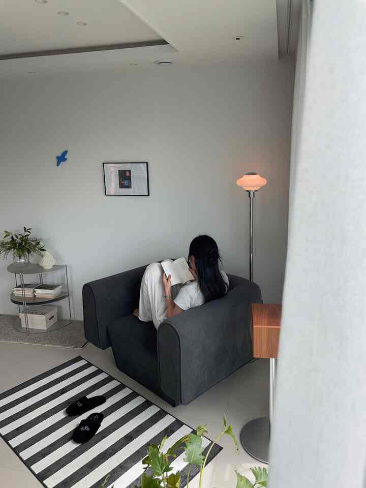 モノトーンのリビング、中央にグレーのファブリックソファとストライプのラグが置かれた、落ち着いた読書スペース