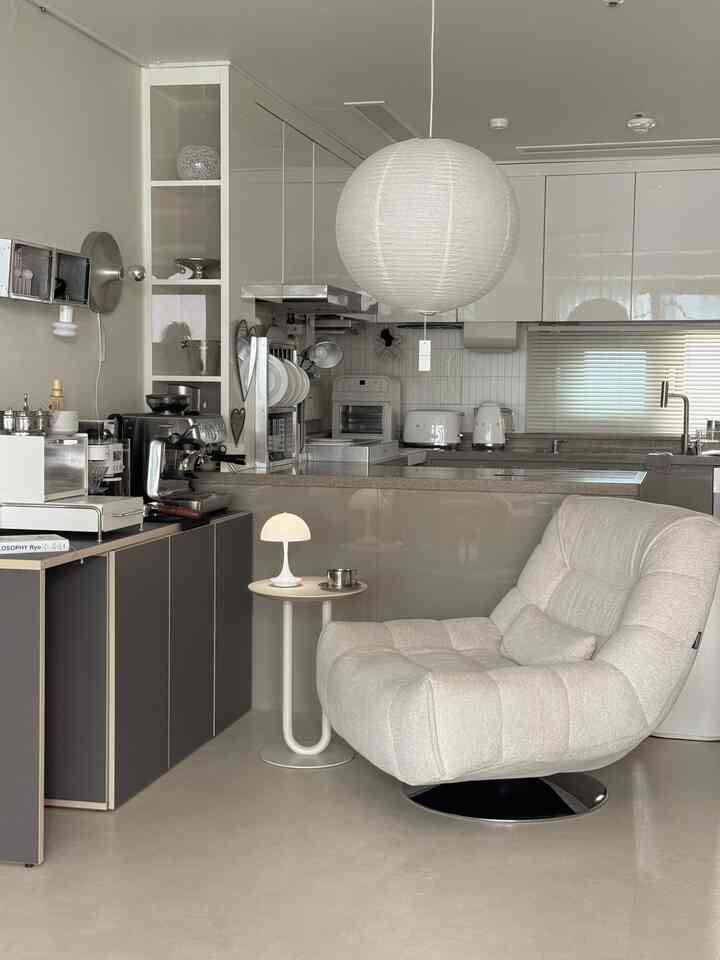 ベージュとホワイトのトーンのキッチン空間、モダンなアームチェアとサイドテーブルが配置されたミニマルなインテリア