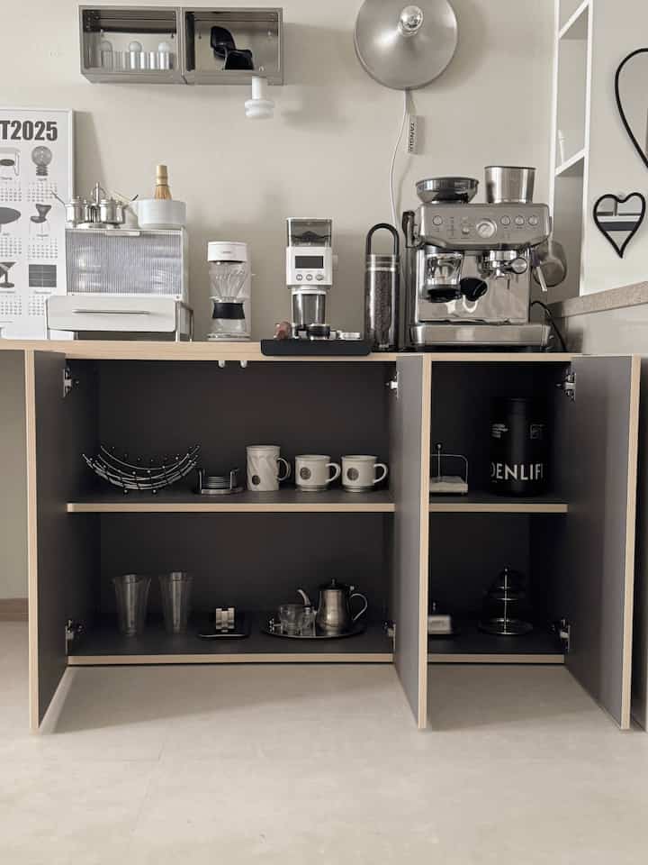 白い壁とベージュの木製カウンターがあるキッチン、シルバーのコーヒーマシンとコーヒー用品が配置された雰囲気のあるおうちカフェ